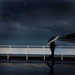 Photograph of a man with an umbrella on Cromer pier taken at dusk.