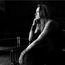 Black and white photograph of a Tattoo Artist with bare arms in a bar.