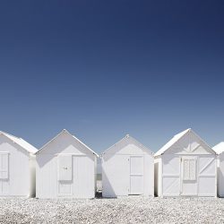 Photograph of white beach huts against a blue sky on the Normandy coast.