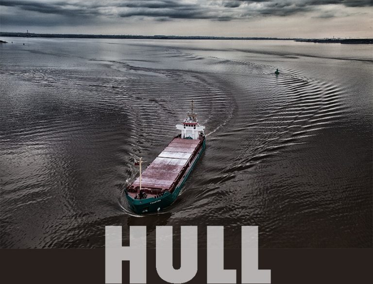 Colour photograph of a ship going under Humber bridge.