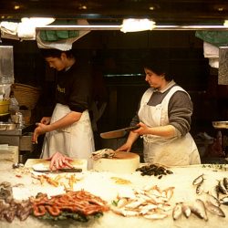 Colour photograph of a Fishwife in Barcelona Fish Market passing a knife.