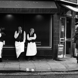 Black and white photograph of waiters outside a bar in London.