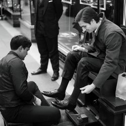 A black and white photograph of a shoeshine at work in London