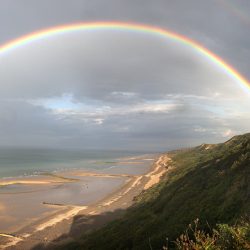 Cplour photograph of a rainbow over the beach near Cromer Lighthouse.