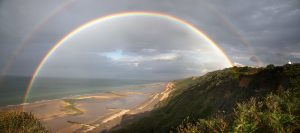 Cplour photograph of a rainbow over the beach near Cromer Lighthouse.