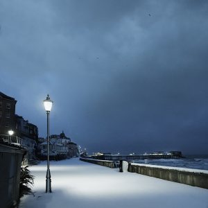 Colour photograph of snowfall on Cromer promenade with lamplight just before dawn.