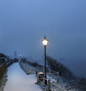 Colour photograph of snowfall over Cromer and lamplights.