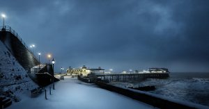 A colour photograph of snowfall on the promenade at Cromer before dawn.