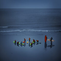 A. photograph of surfers on the beach in luminous wet suits and paddle boards