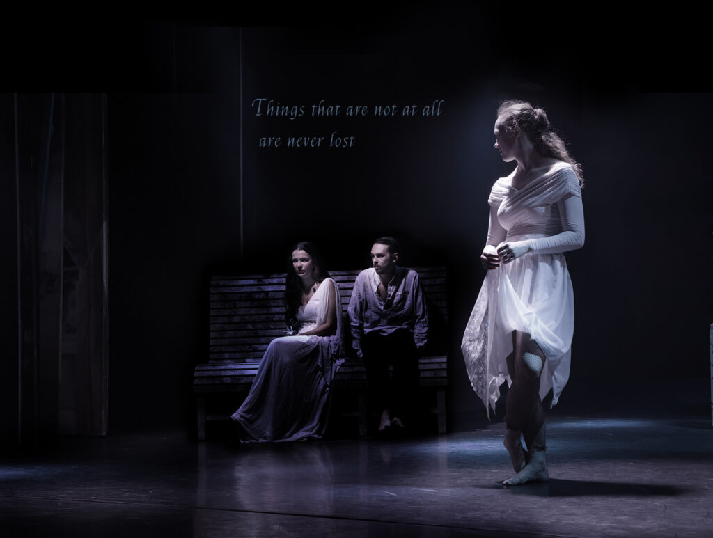 A young woman dancer stares intently at a couple sat deep in shadow on a bench. Something is happening.