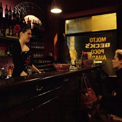 Photograph of a barmaid in an exotic dress and another girl talking.