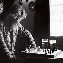 Black and white photograph of two men play chess in a pub.