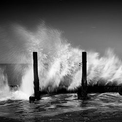 Black and white photograph of waves pounding old wooden sea defences on the Norfolk coast.