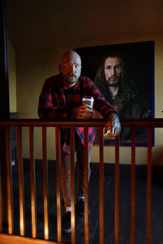 A man with a drink in front of a painting The Suffield Arms Norfolk.