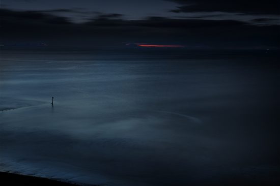 Photograph of the sea at dusk with a red strip of the setting sun on the horizon