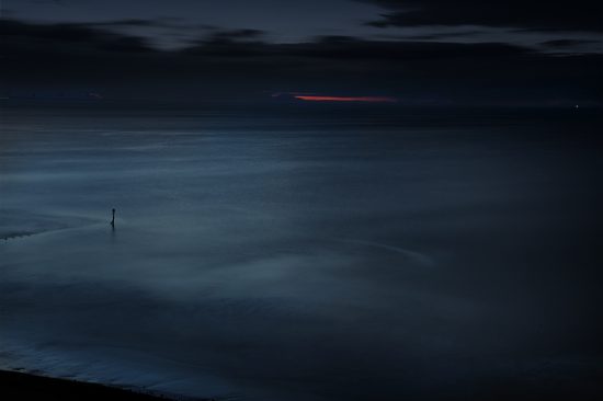 Photograph of the sea at dusk with a red strip of the setting sun on the horizon
