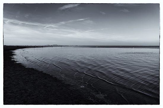 Tri tone photograph of a bleak looking sea shore and people in the far distance